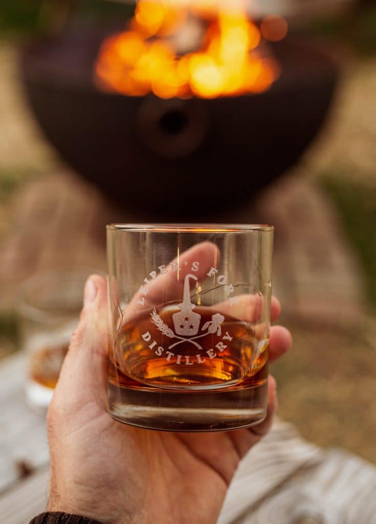 A Leiper's Fork Distillery rocks glass of whiskey held up in front of a glowing fire pit