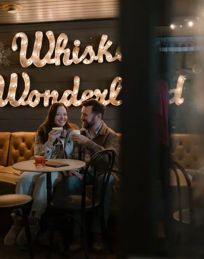A couple toasting with seasonal cocktails in a leather booth beneath a lit marquee sign
